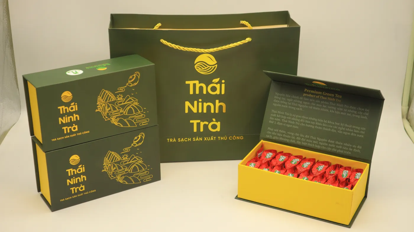 Hai hộp quà đóng, một hộp mở với các gói trà và túi xách quai bện Thái Ninh Trà
