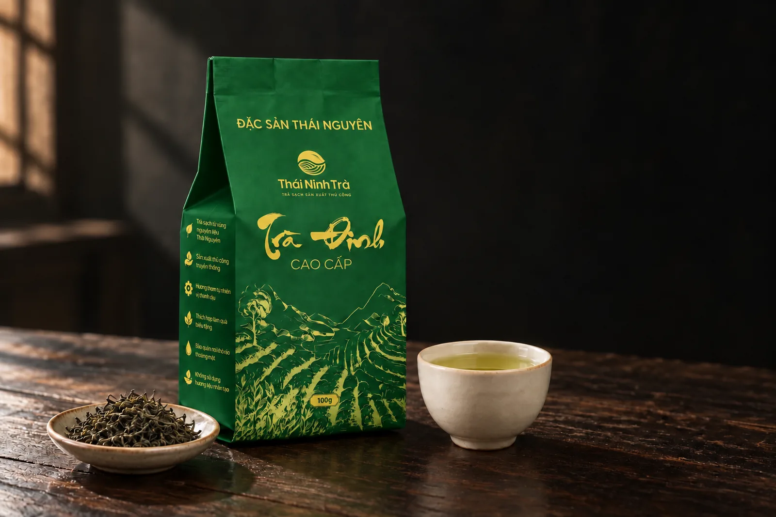 Gói Trà Đinh Cao Cấp bên chén trà nước xanh vàng trên bàn gỗ